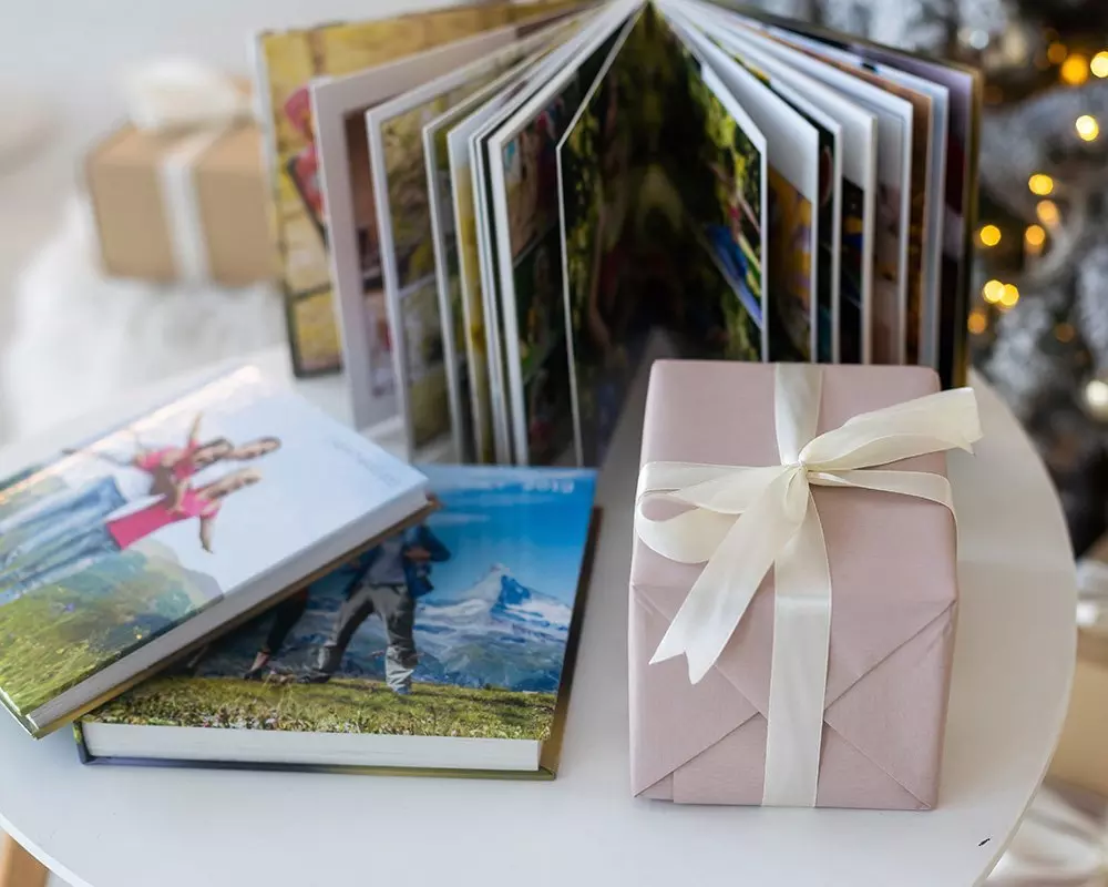 Photo albums and a pink gift box with white ribbon from Pepco displayed on a white table with festive lights in background.