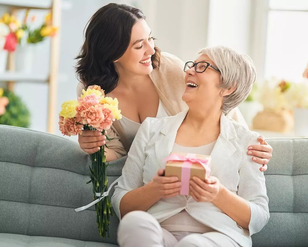 Two women sharing a joyful moment with Pepco gifts - colorful flowers and a wrapped present with pink ribbon.