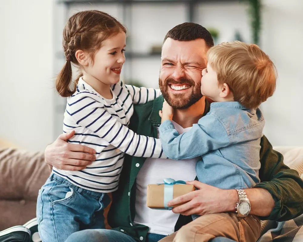 Happy family moment with children hugging adult who holds a Pepco gift box with blue ribbon.