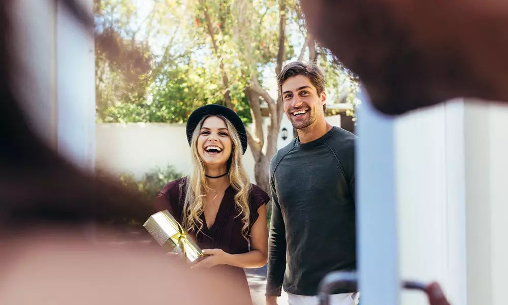 Two people smiling outdoors, one wearing a black hat and holding a gold gift from Pepco.
