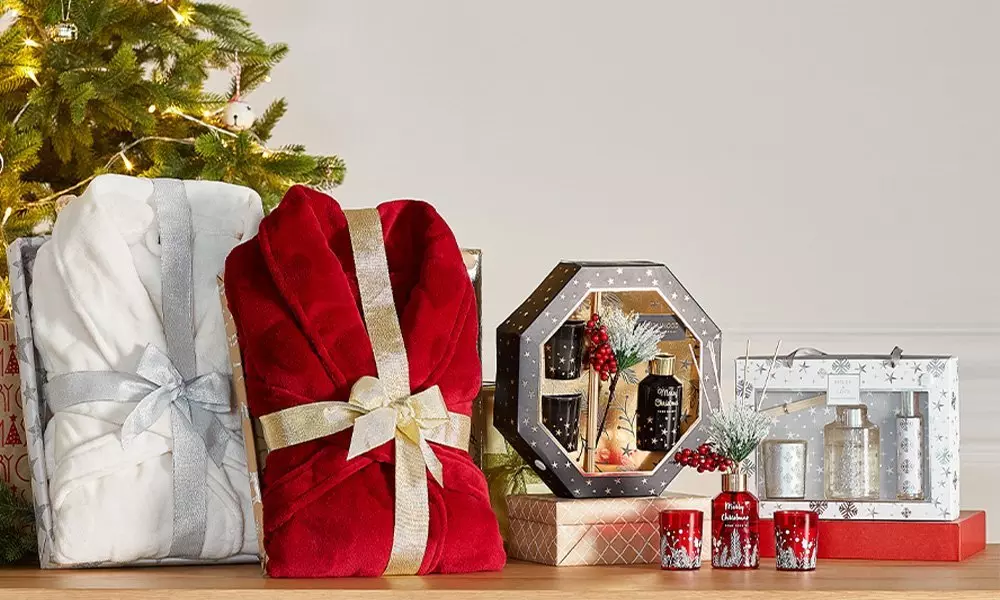 Świąteczne prezenty Pepco: białe i czerwone szlafroki, zestawy kosmetyków w ozdobnych pudełkach i świeczki pod choinką.