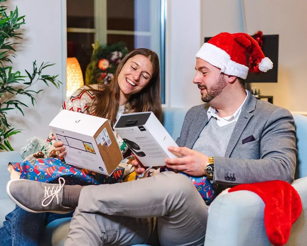 Para otwierająca prezenty świąteczne, mężczyzna w czapce Mikołaja, kobieta w świątecznym swetrze, produkty Pepco.