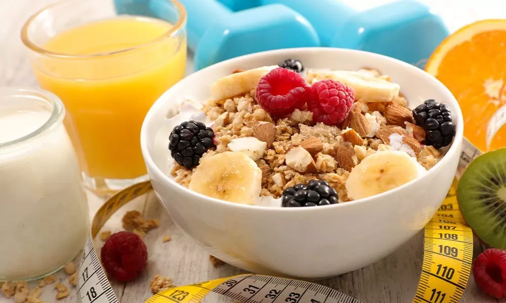 Bol Pepco cu cereale, fructe și nuci, alături de suc de portocale, lapte și o ruletă de măsurat, pentru un mic dejun sănătos.