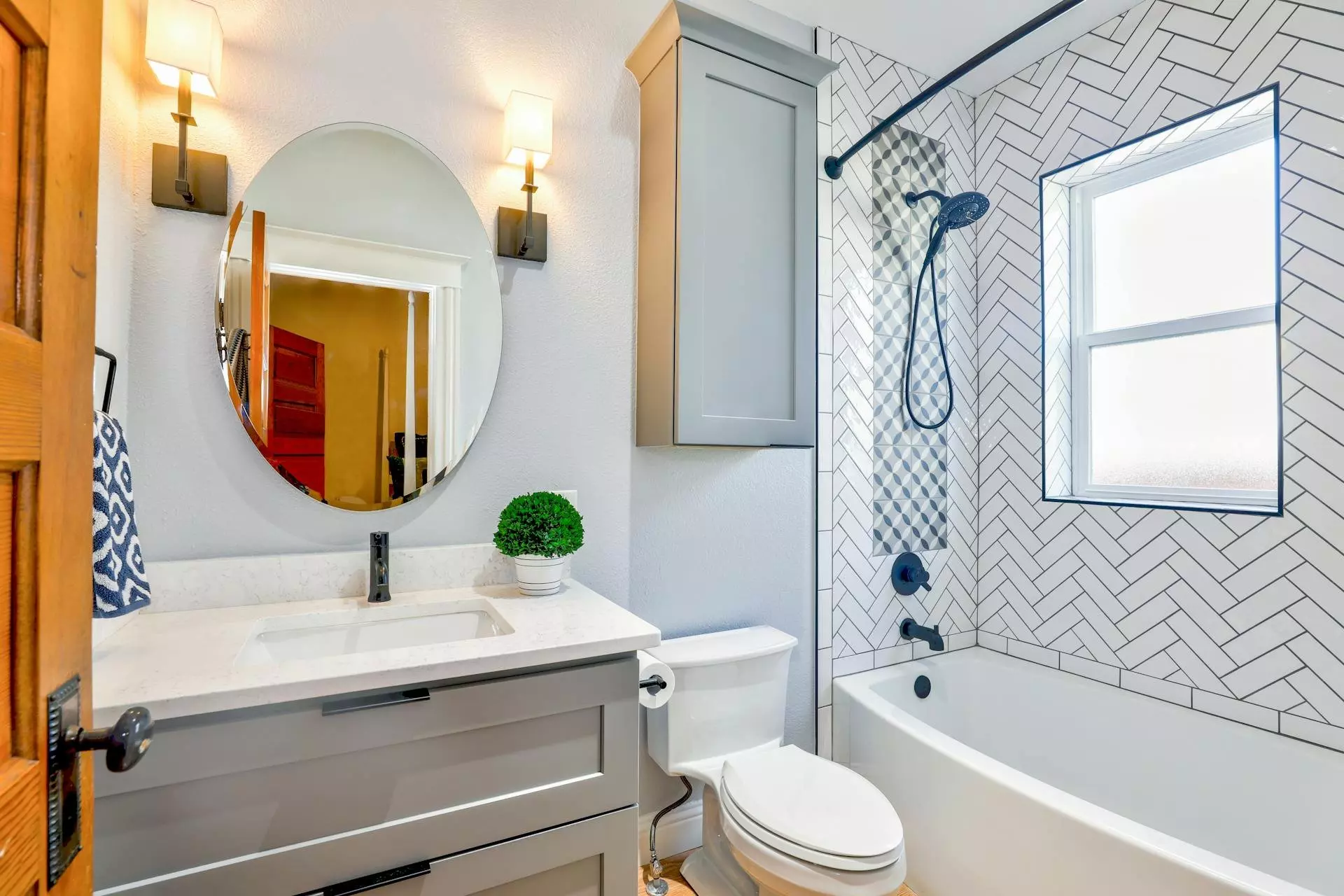 Bagno moderno con mobile lavabo grigio, specchio rotondo, piastrelle a spina di pesce e vasca-doccia.