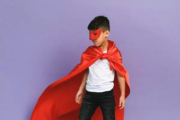 Bambino Pepco indossa un costume da supereroe con mantello rosso e maschera in posa eroica.