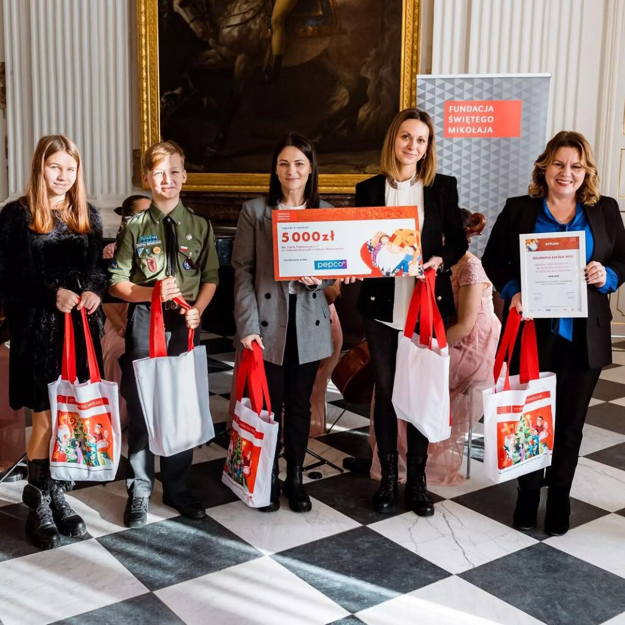 Group at charity event displaying Pepco's 5,000zł donation check to Fundacja Świętego Mikołaja, holding branded tote bags.