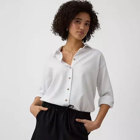 Kobieta w białej koszuli z guzikami i czarnych spodniach z wiązaniem w talii.