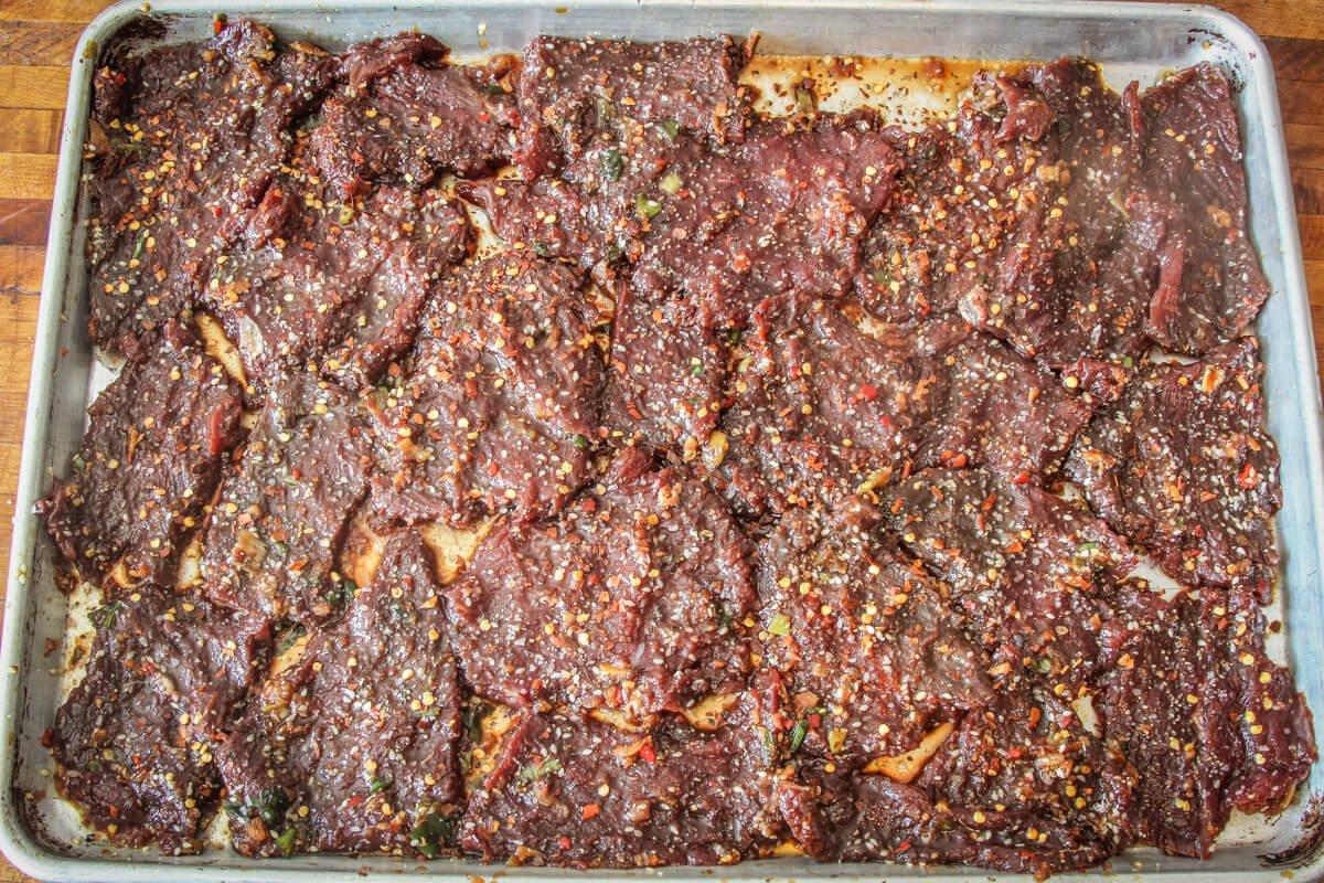 Spread the jerky flat and sprinkle with more sesame seeds and red pepper flakes before drying.