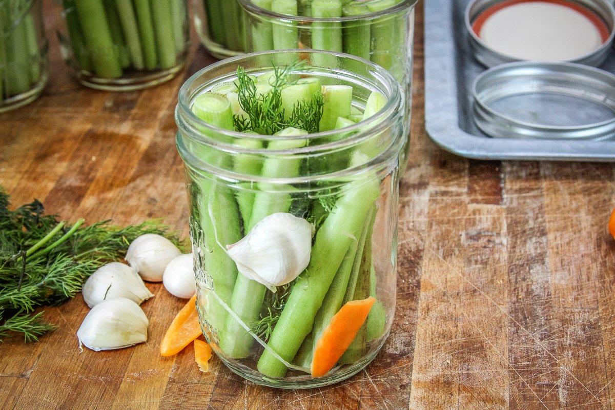 Fill the sterilized jars with cattail stalks, then add garlic, fresh dill and a wedge of habanero pepper.
