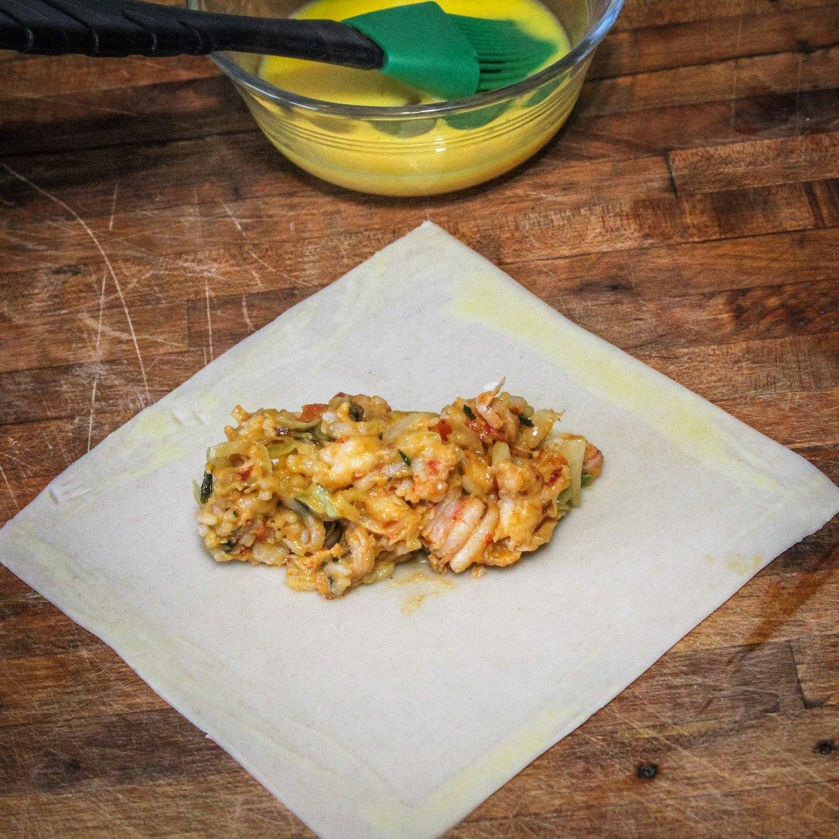 Brush the edges of the egg roll wrapper with egg wash and spoon filling to the center.