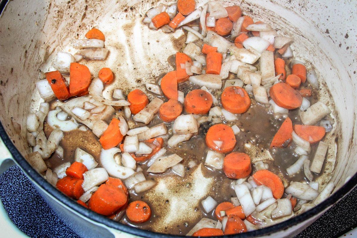 Once the meat has been browned, add the onions and carrots to the pot to soften.