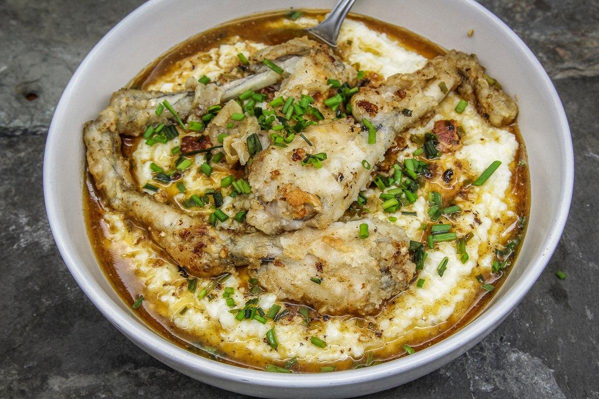 Add the frog legs to the top of a bowl of cheese grits, then spoon over some sauce.