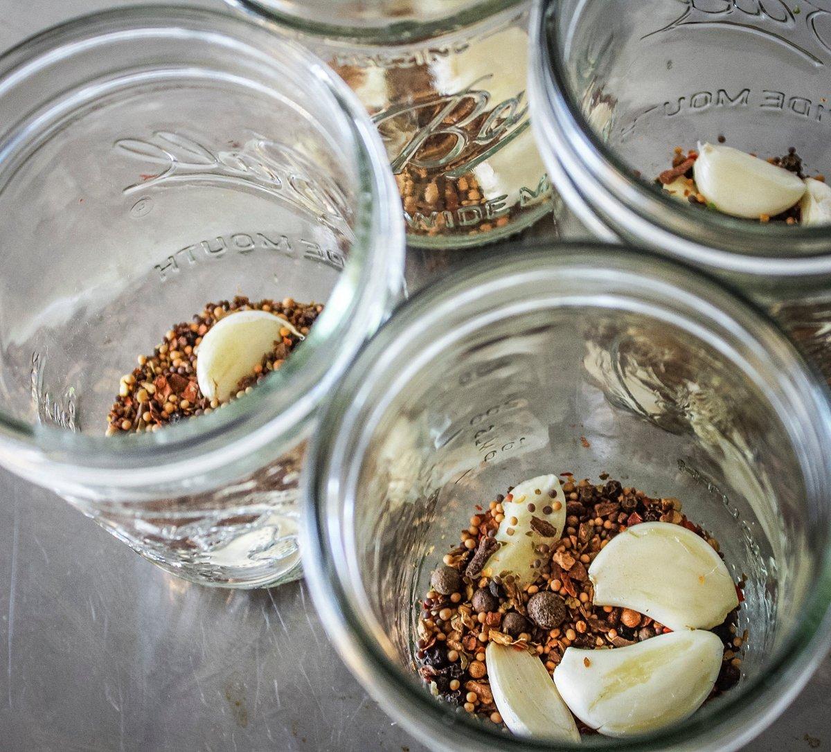 Add the garlic cloves and seasoning to the bottom of each jar.