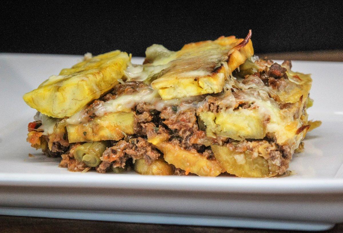 The dish features layers of fried plantain, vegetables, and meaty sauce, all held together by lots of melted cheese.