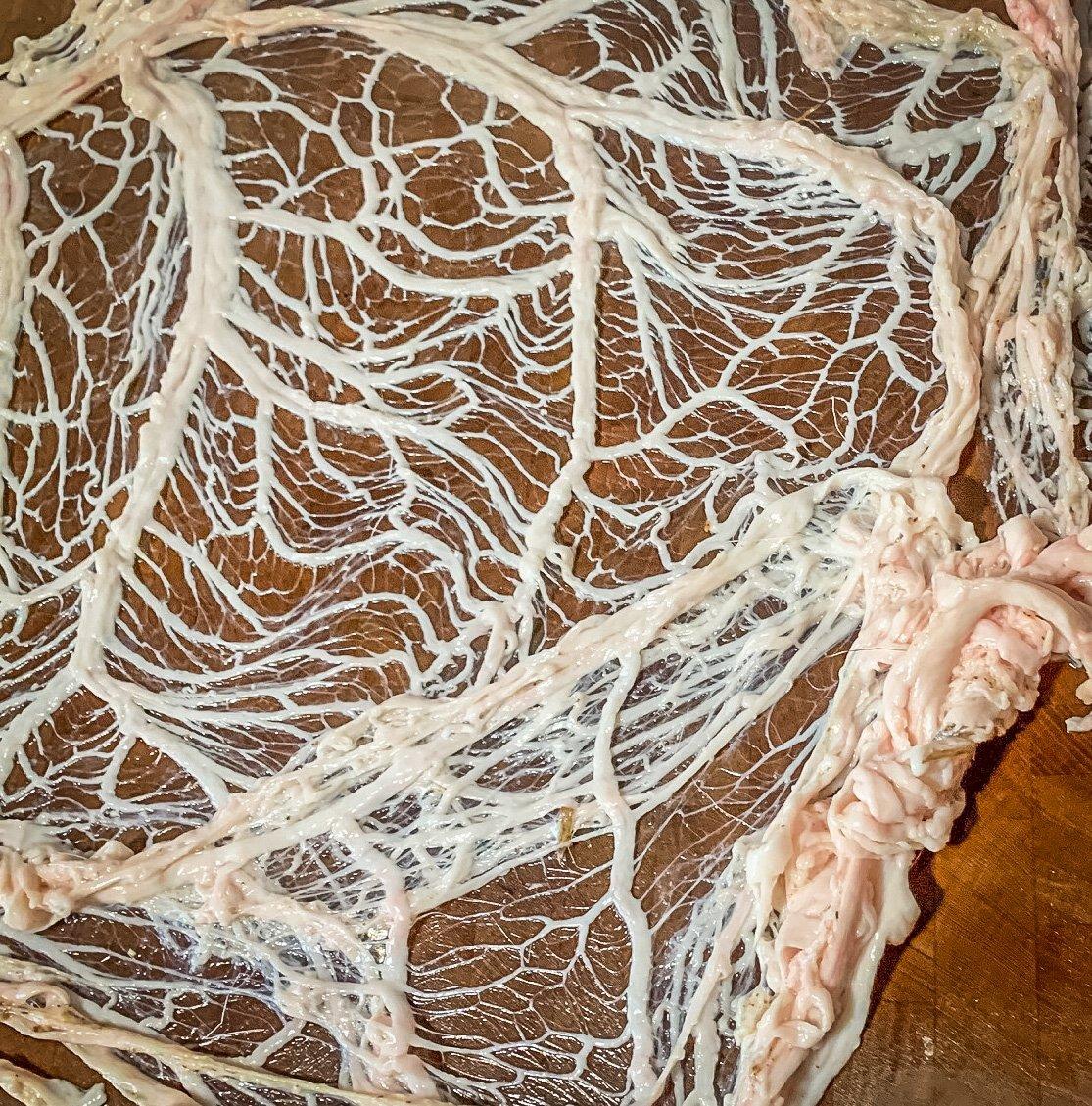 Caul fat peels away in a large, lacy sheet.