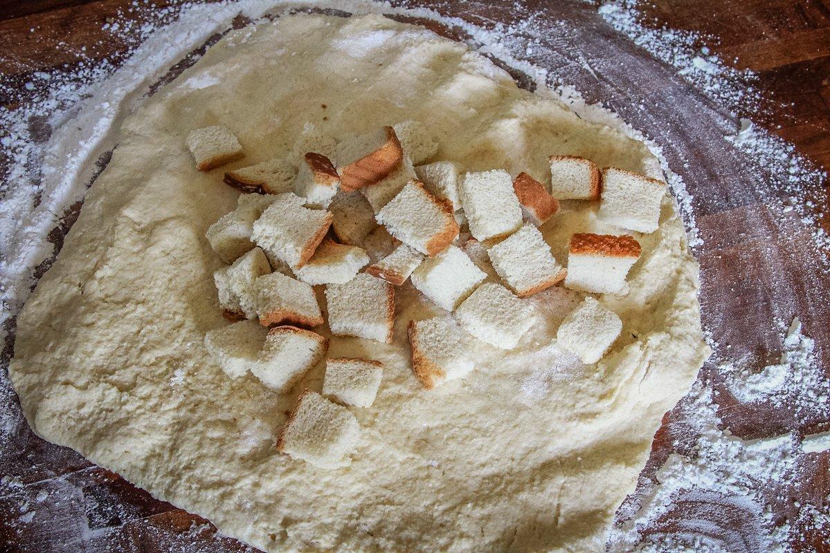 Flatten the dough onto a floured surface and add the dried bread to the center before kneading into a ball.