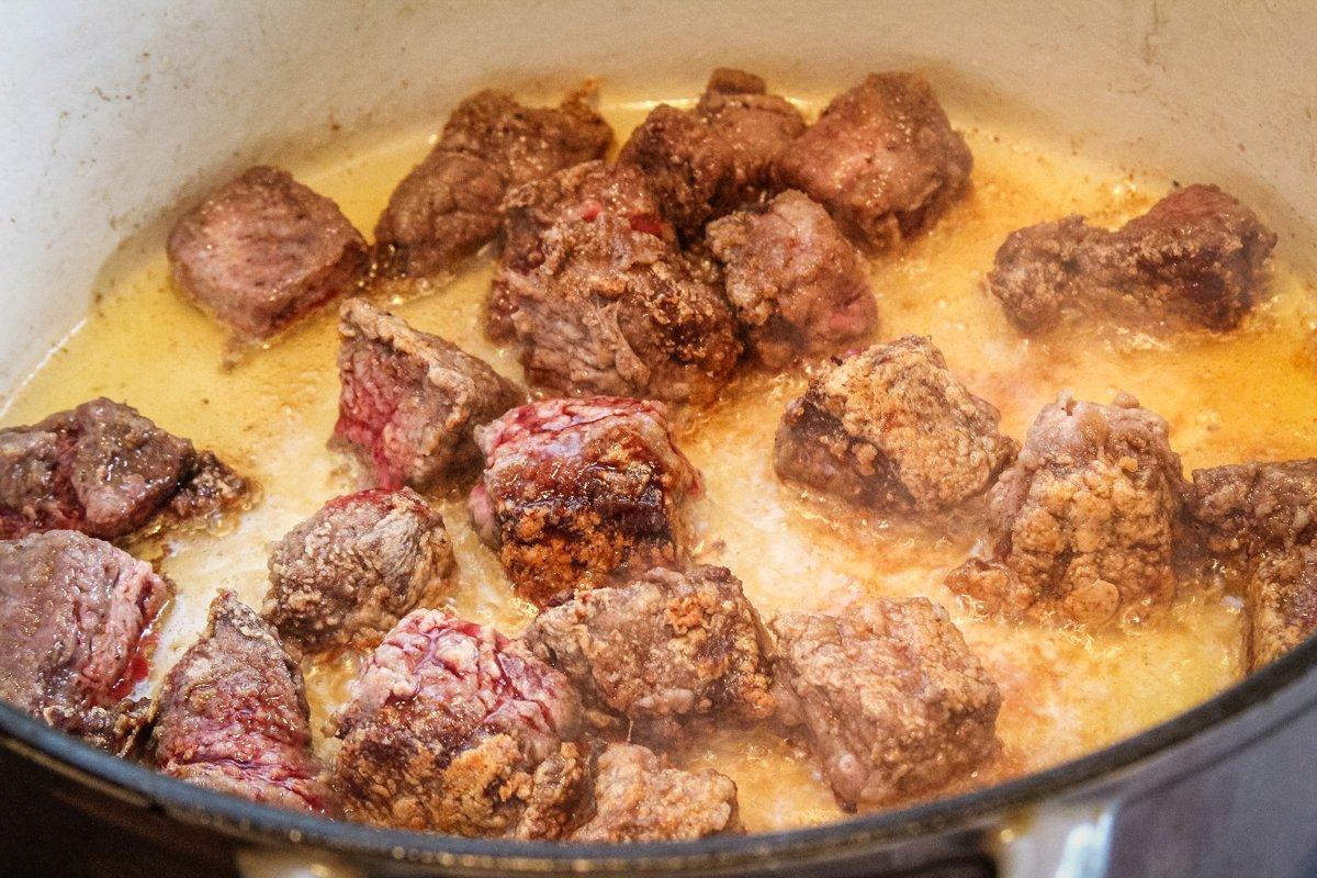 Brown the floured venison pieces in hot oil.