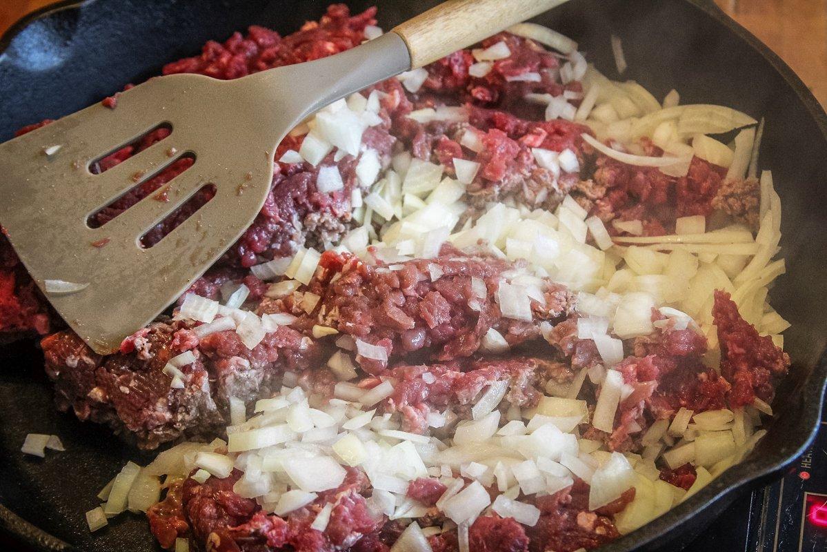 Start by browning the ground venison with chopped onion in a large skillet.