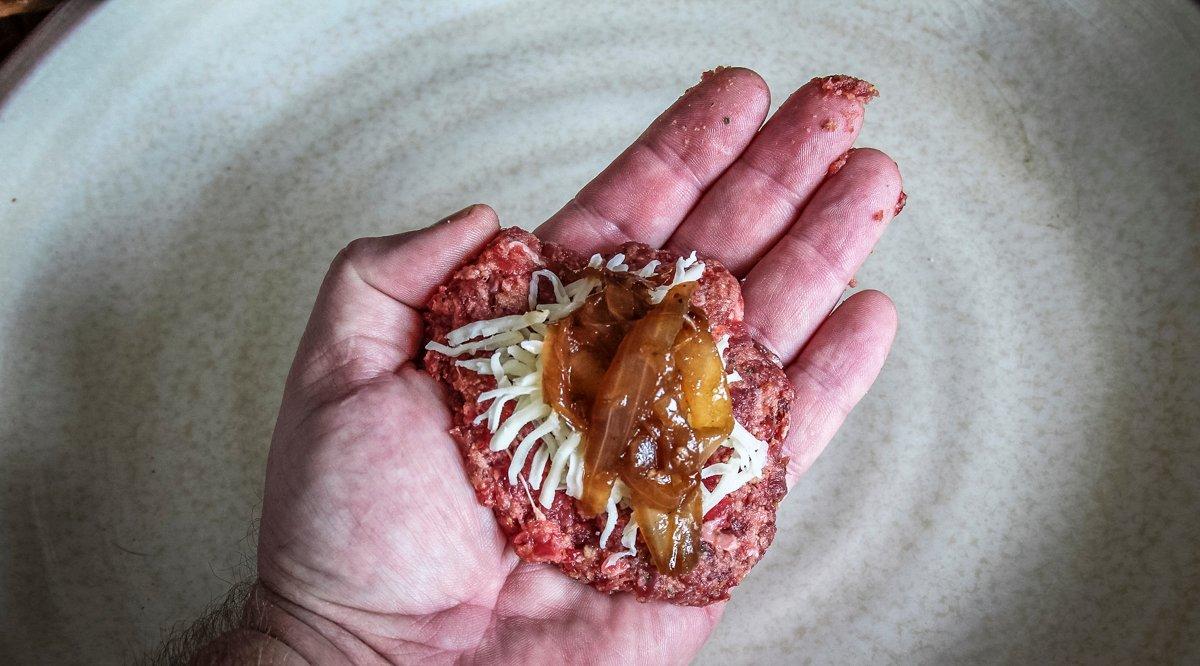 Flatten a ball of meat mixture in your hand and spoon on some onion and cheese before closing up the meatball.
