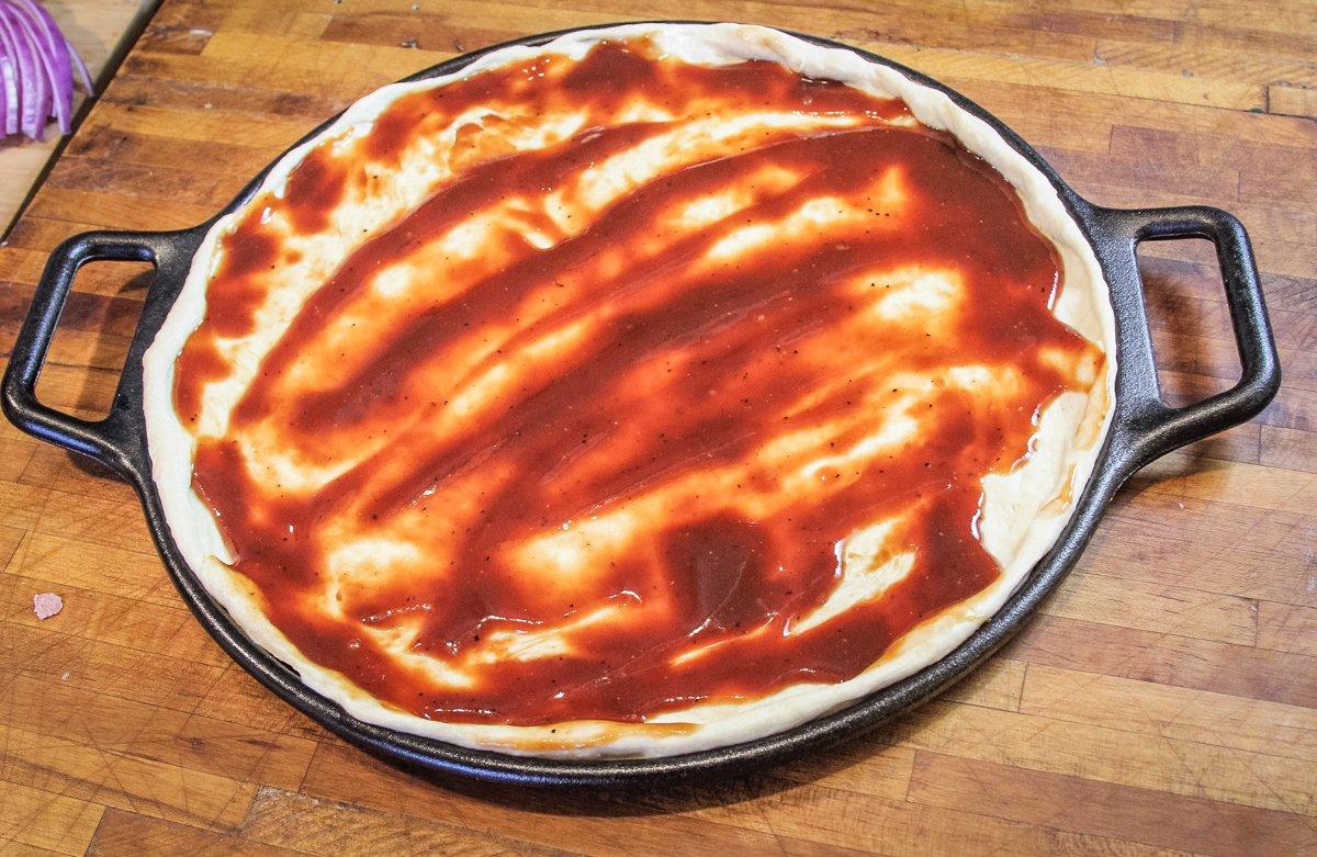 Spread the pizza dough on the Lodge baking sheet, then spread on the sauce.