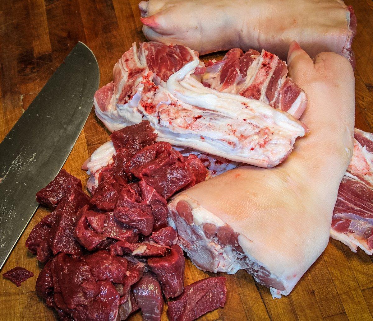 Start by cutting the venison into cubes and splitting the pork shanks down the center.