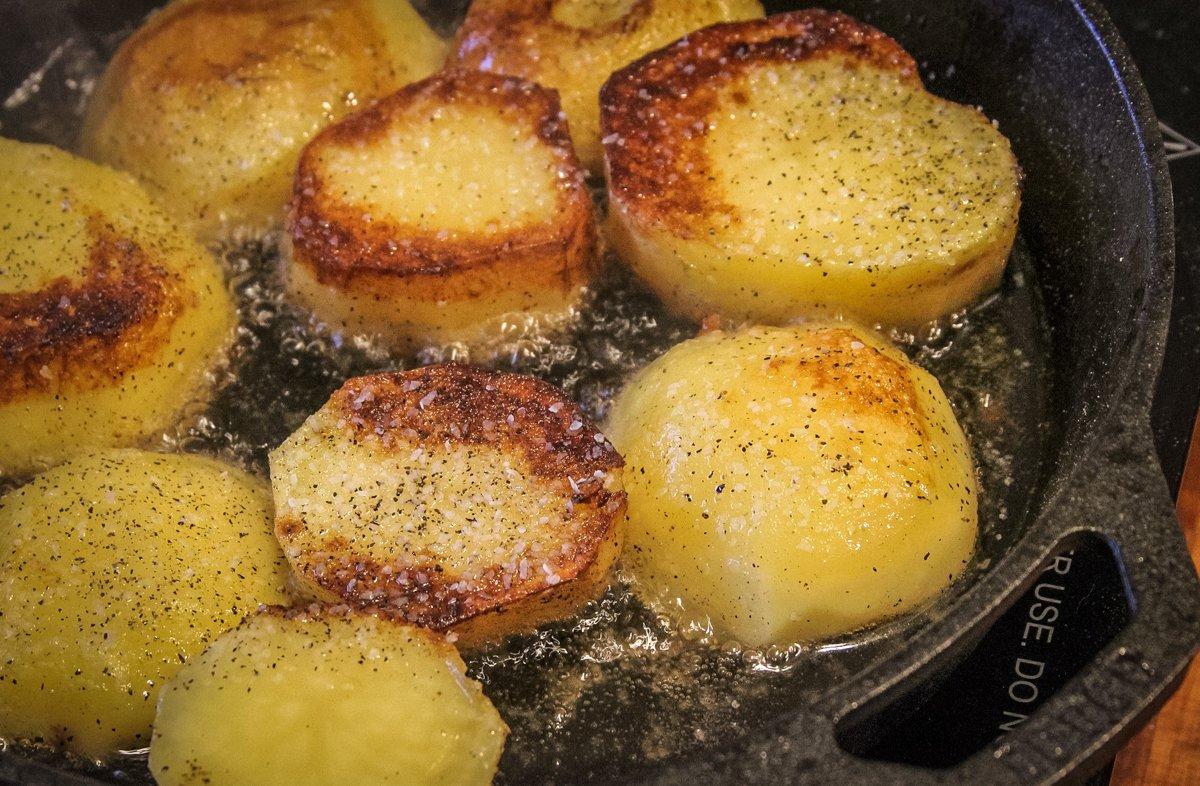 Season the potatoes with salt and cracked black pepper, then brown in duck fat.
