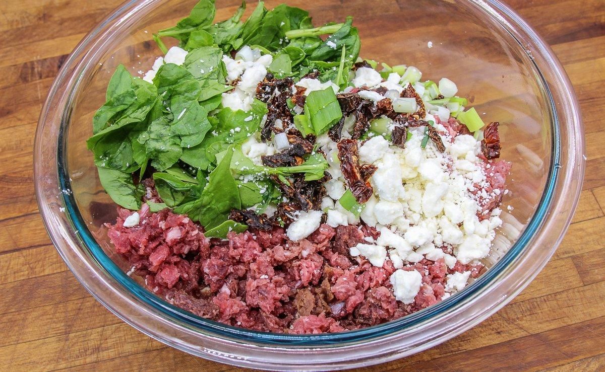 Add the sun-dried tomatoes, feta cheese, green onions, and spinach to the ground venison.