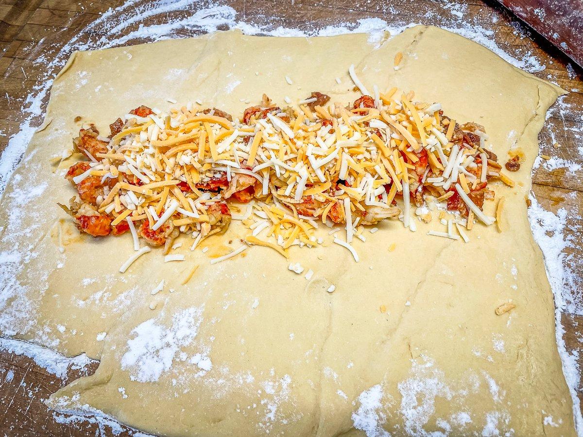 Drain any cooking liquid from the pan before adding half the crawfish filling to the rolled dough sheet. Top with cheese.