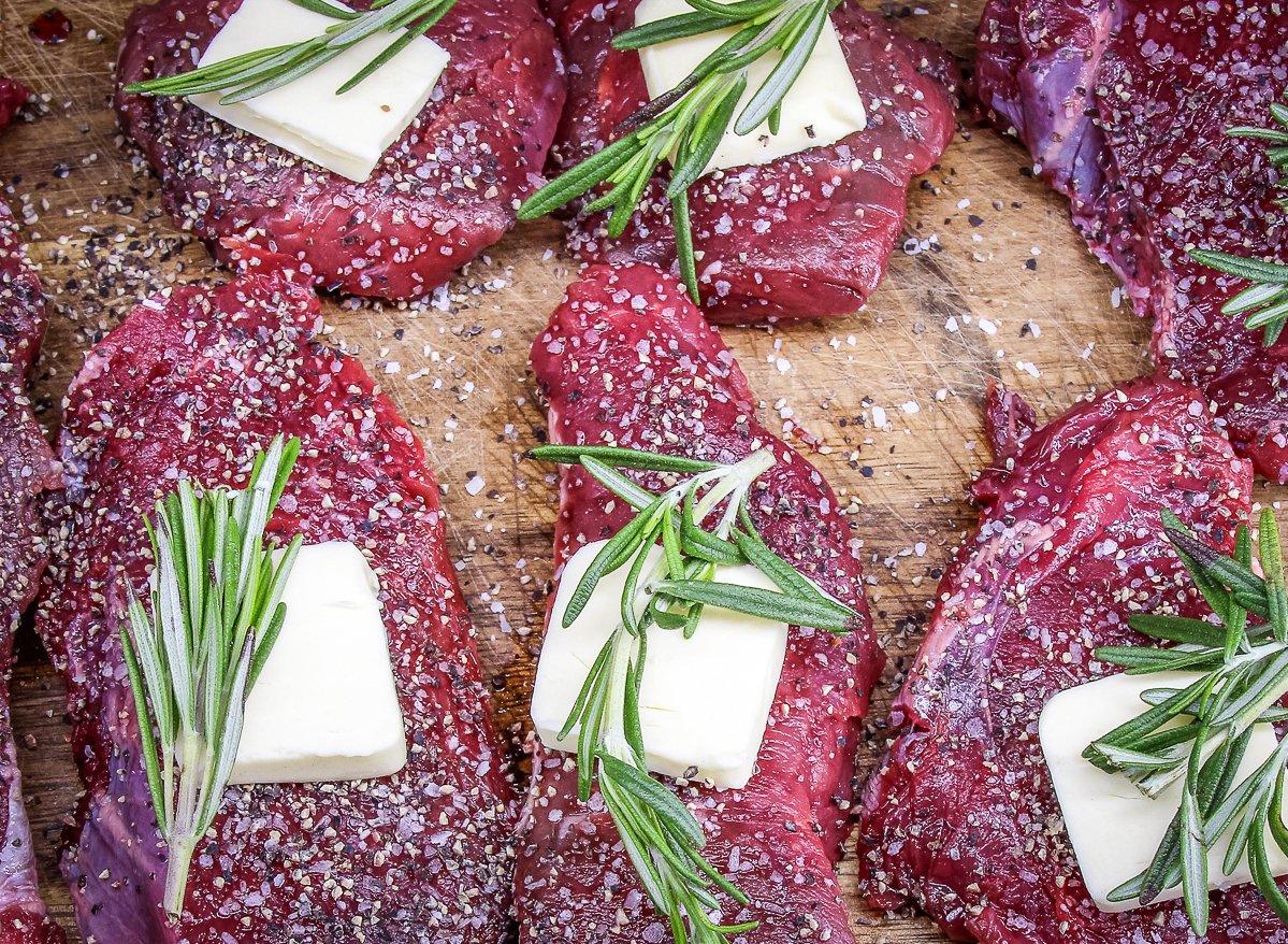 Season each steak with salt and pepper, then top with a pat of butter and a sprig of rosemary.