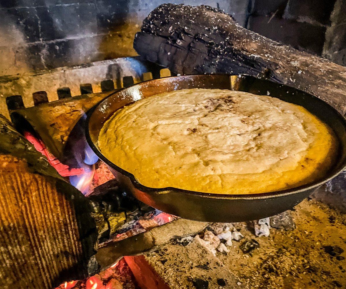 Adjust coals and fire logs to keep the cornbread cooking evenly.