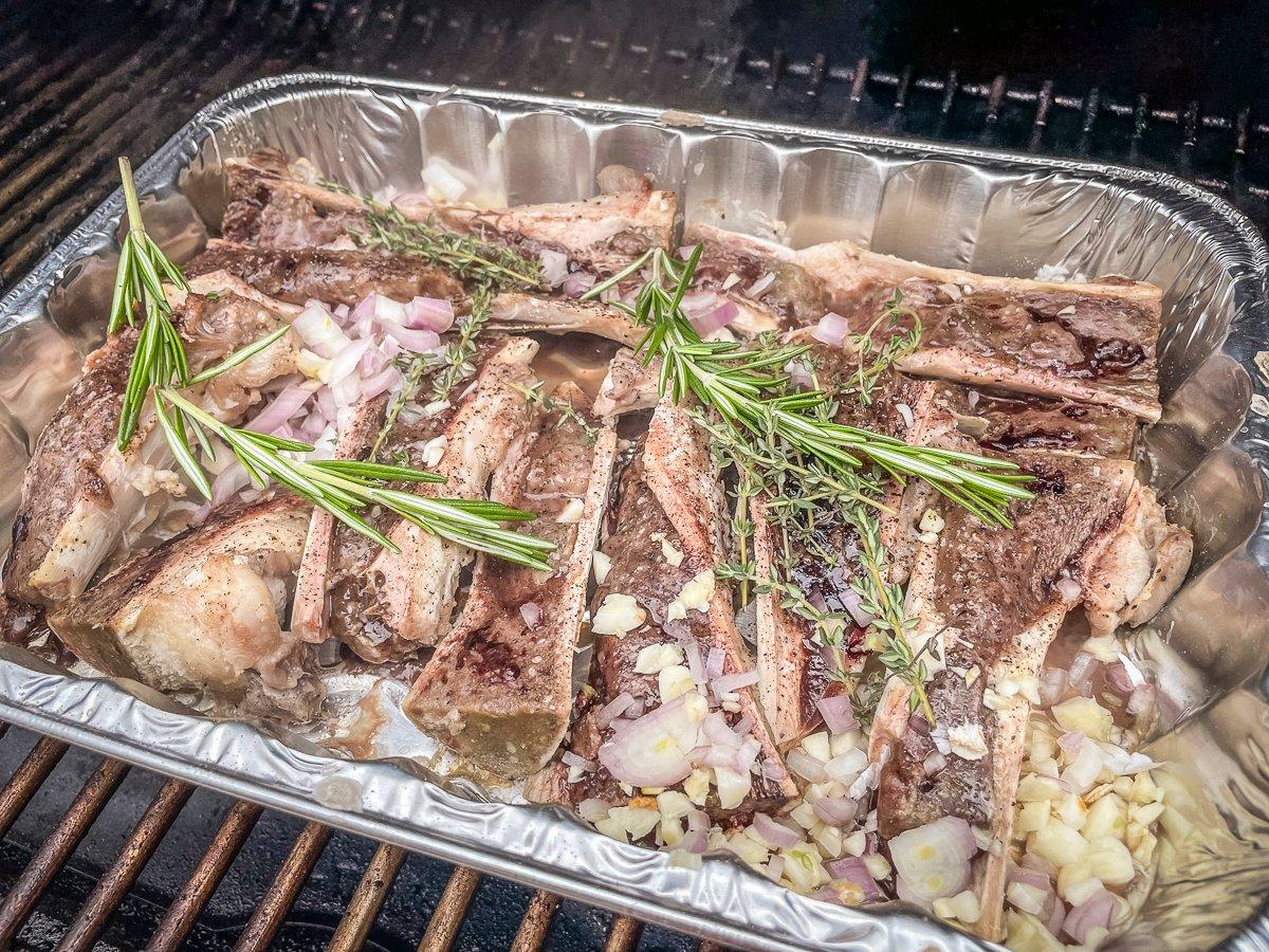 Add the shallot, garlic and fresh herbs to the bones and continue roasting on the grill.