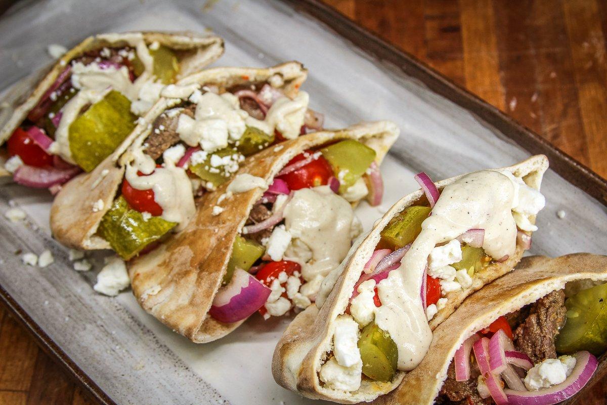 Fill the pita pockets with grilled venison, tomato pickle salad, and feta cheese, then drizzle on tahini sauce before serving.