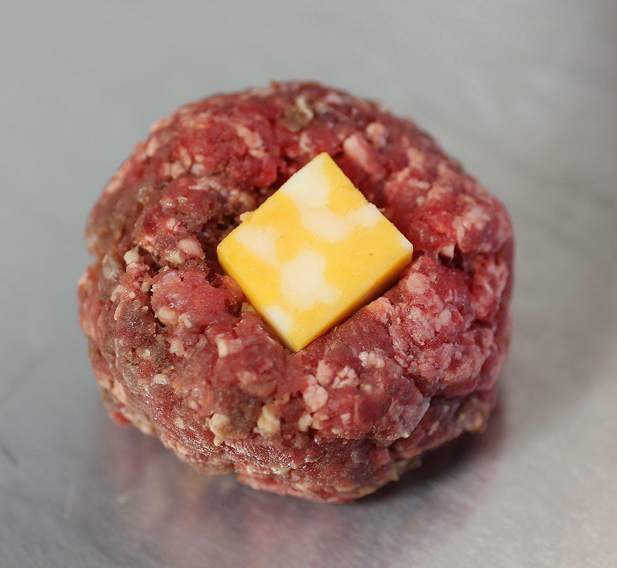 Cover a cheese cube with ground meat and roll into a ball.