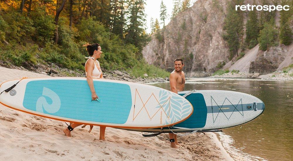 two people carrying paddle boards to the water