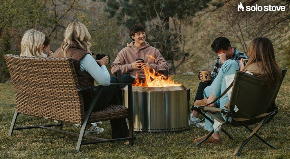 a group of people sitting around the Solo Stove in a backyard