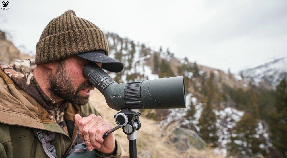 a hunter looking through a spotting scope in the mountains