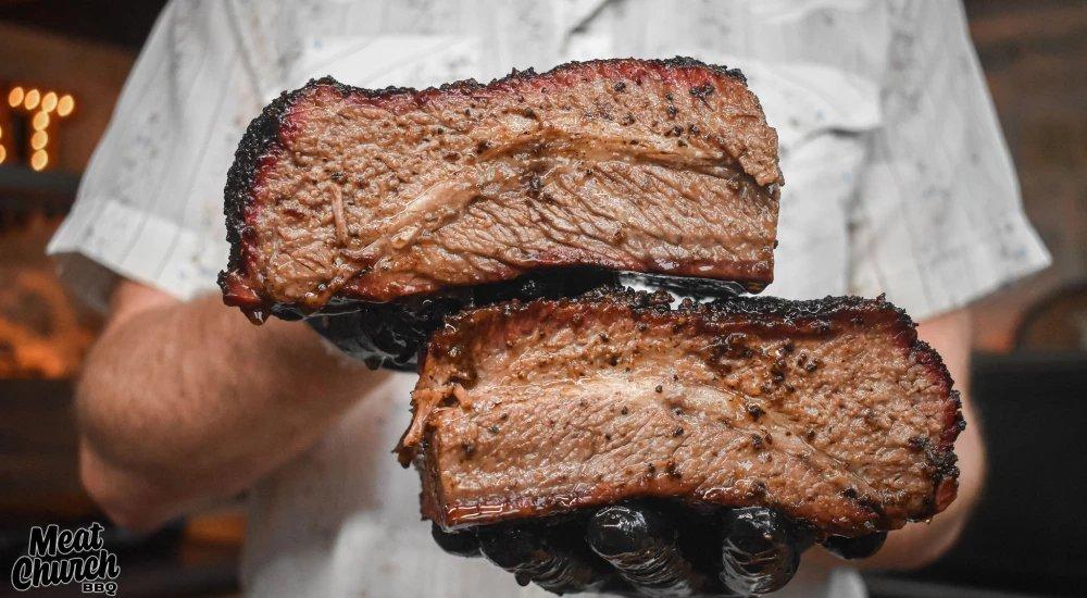 a man holding up meat that has been seasoned and grilled