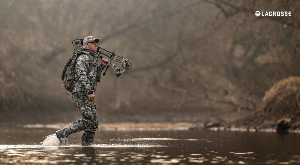 a hunter walking through water while holding a compound bow