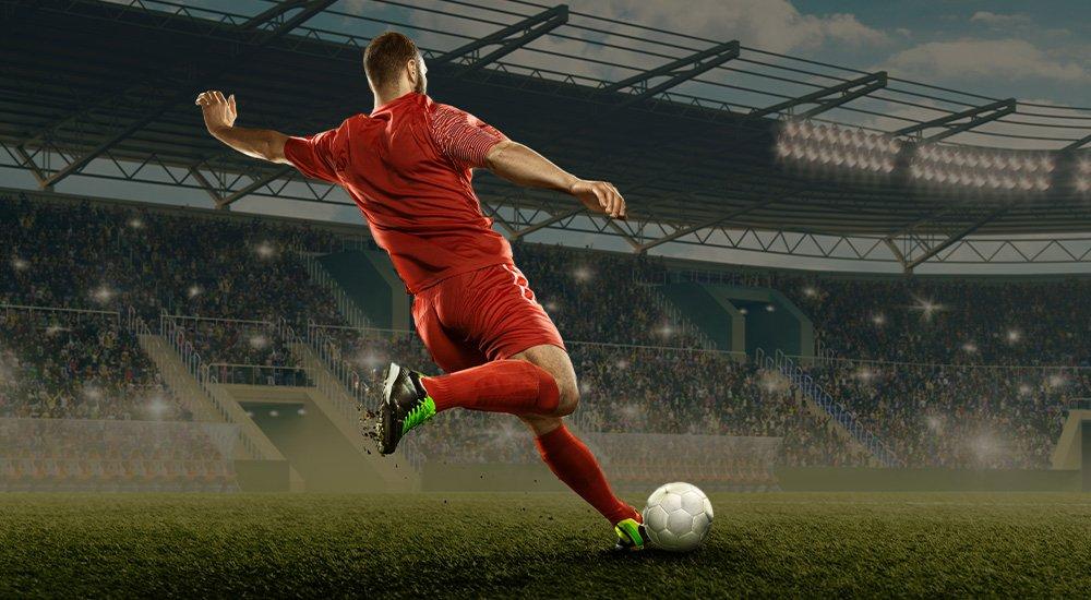 soccer player wearing a red uniform and kicking a ball in a stadium