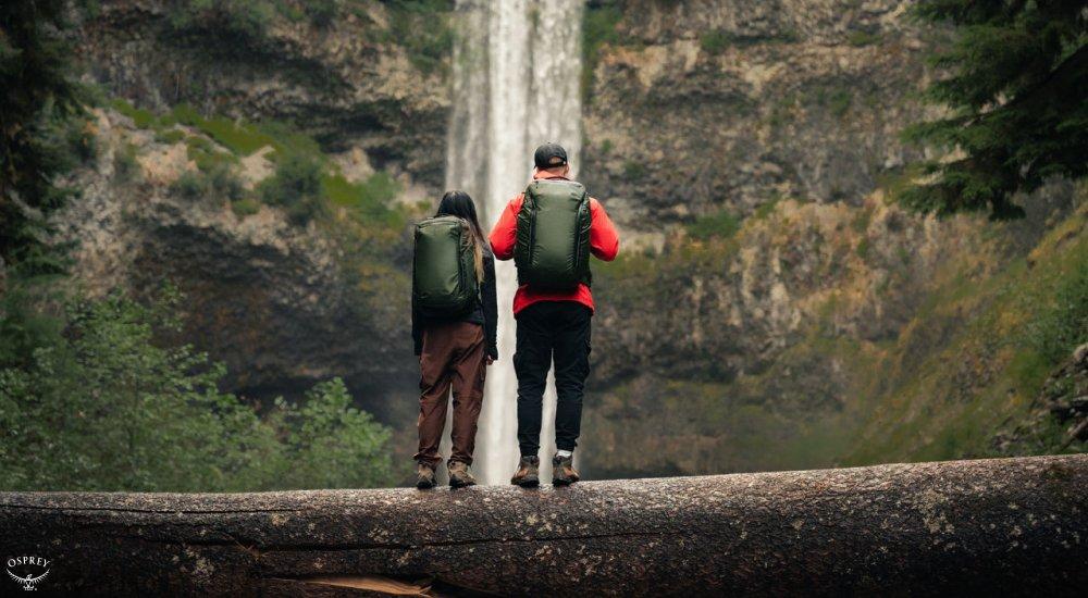 two people standing on the trail looking at a waterfall