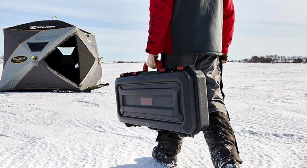 an ice angler carrying a hard sided ice rod case to the shelter