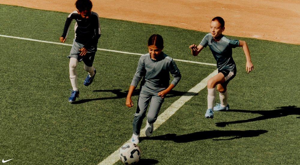 three kids running down the soccer field with a soccer ball