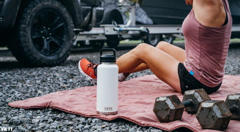 a woman stretching with a pair of dumbbells and a YETI water bottle next to her