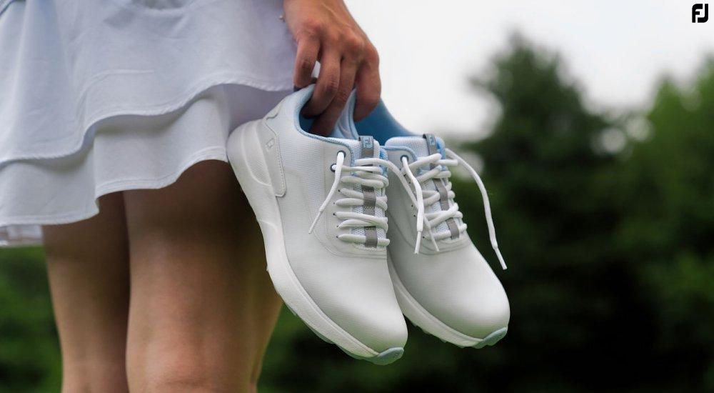 a female golfer holding a pair of golf shoes on the course