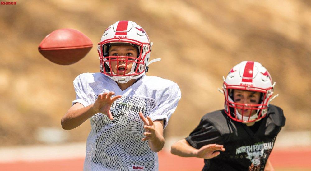 two players wearing shoulder pads during practice and catching a football