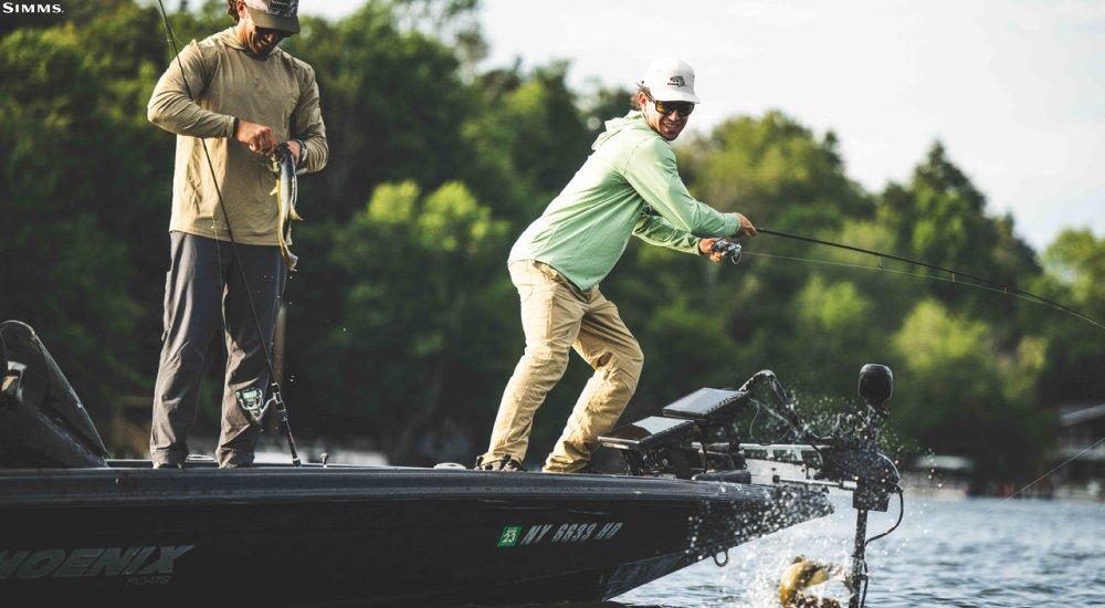 two men fishing on a boat wearing fishing clothing