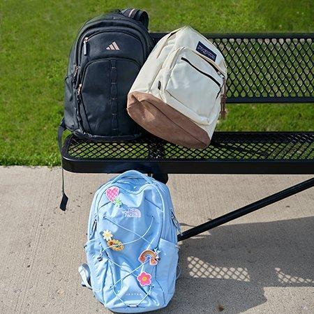 a variety of backpacks on a park bench