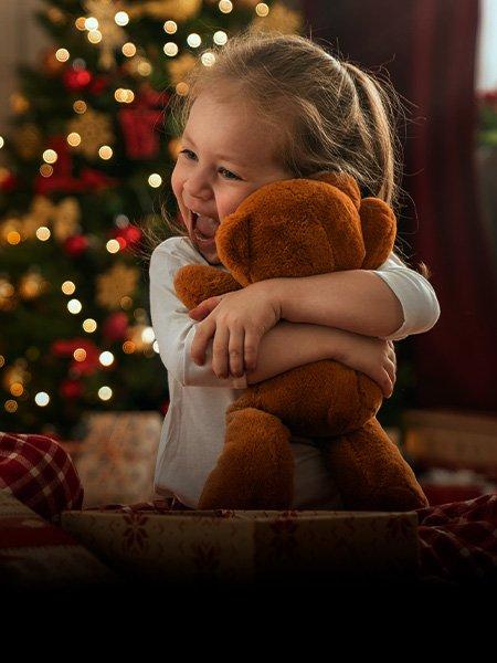 Toddler hugging teddy bear by Christmas Tree