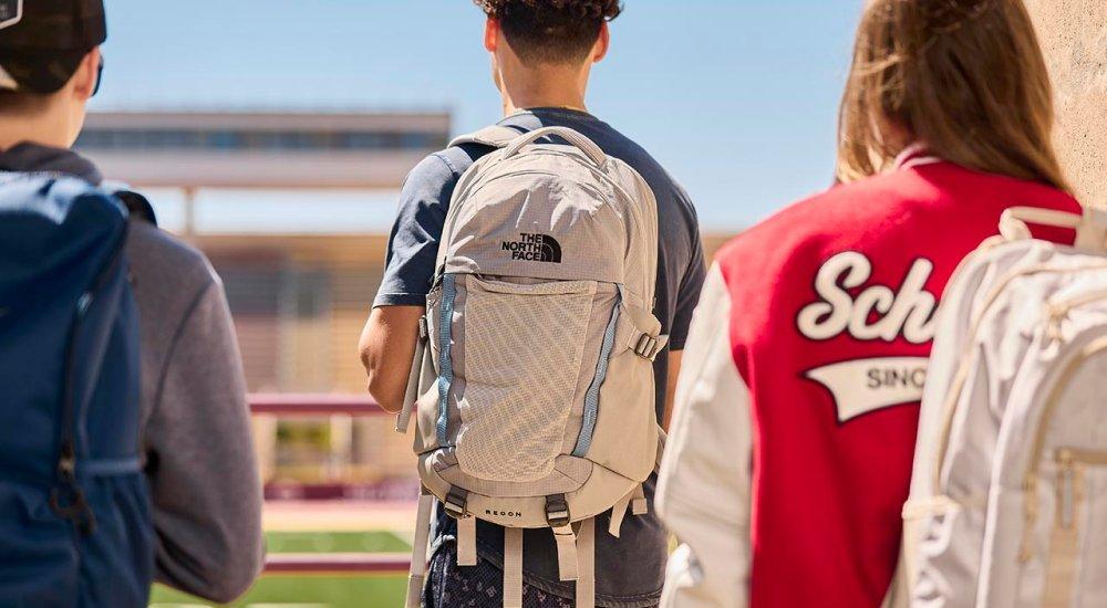 three students with backpacks looking over a football field