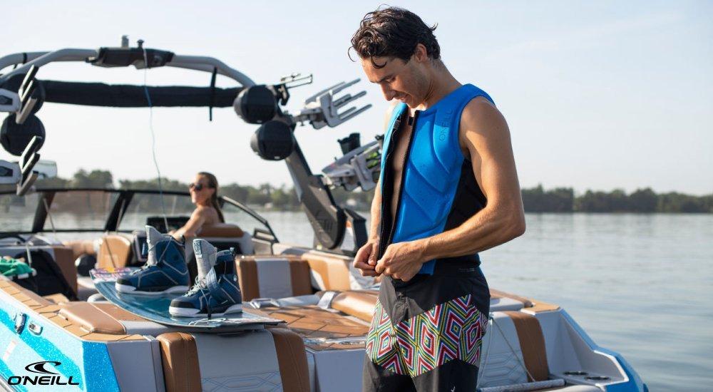 man zipping up life jacket on the back of a boat